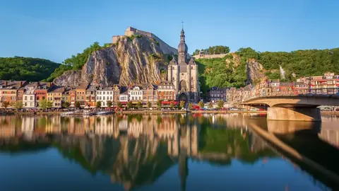 Dinant weerspiegeld in de Maas, met de citadel en de kerk tegen de rotswand
