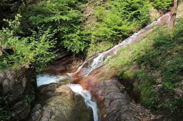 Het water van de Ninglinspo kronkelt over roodbruine rotsen in het bos