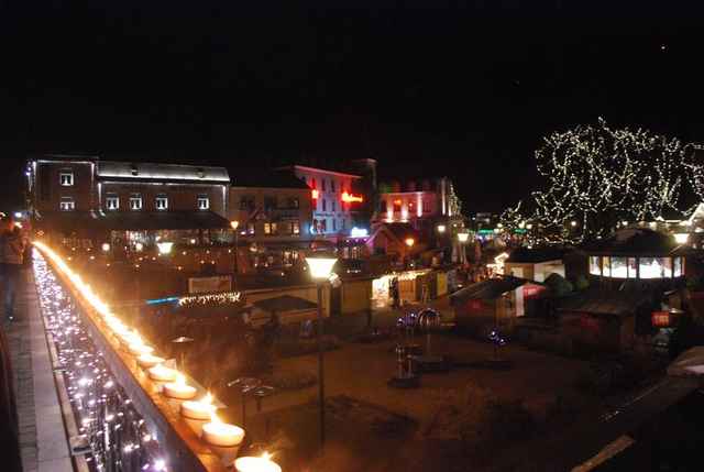 Avondsfeer op de kerstmarkt van Durbuy: een verlichte brug en kraampjes langs het water