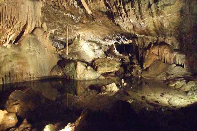 Opplyst dryppsteinshall med en liten underjordisk innsjø i Grottes de Hotton
